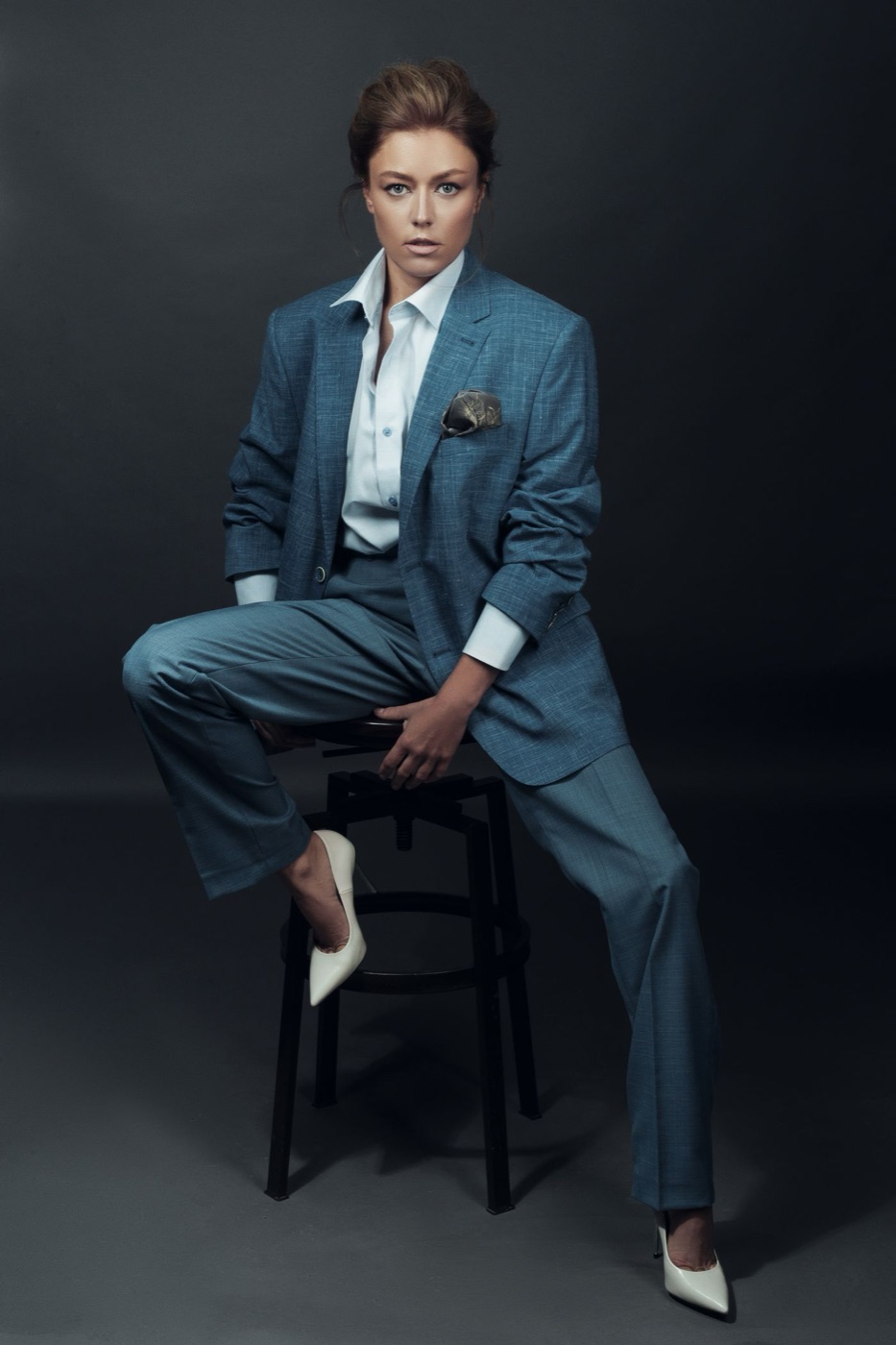 Woman in a blue suit seated on a stool in a dark studio