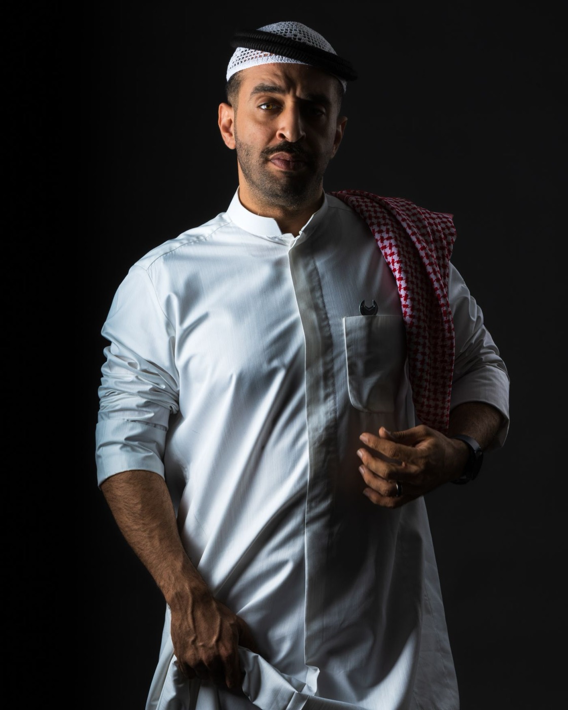 Man in a white thobe and red shemagh in a dark studio